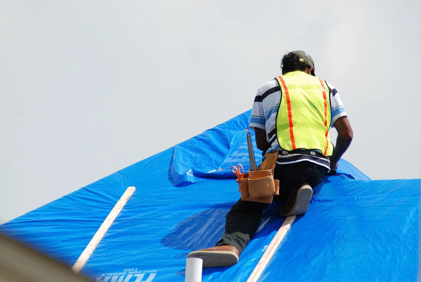 Crew member securing a blue tarp with wood battens on a storm-damaged roof – Hurricane Isaias roof tarp